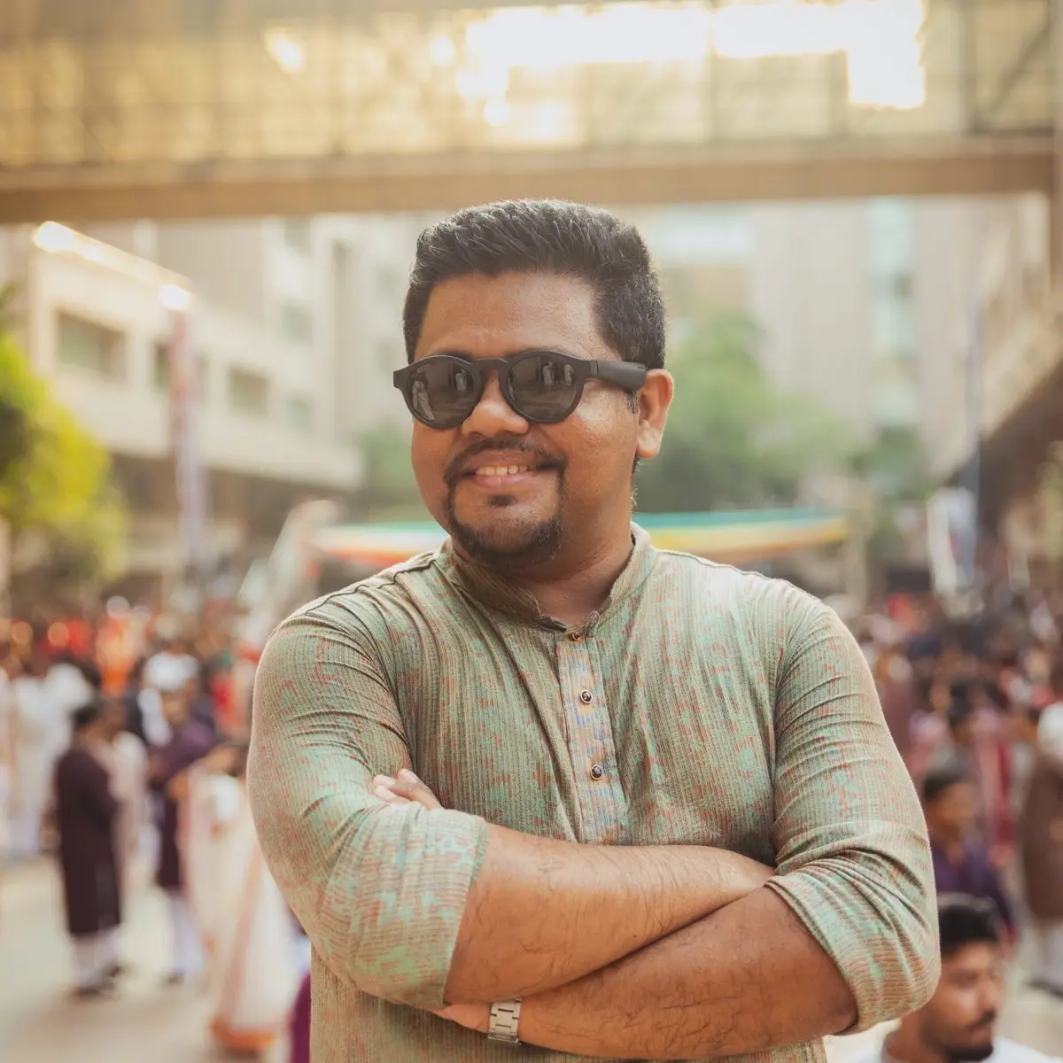 J S Mahboob smiling in a sunlit city crowd